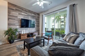 A modern living room with a flat-screen TV, a wooden accent wall, a sofa, a coffee table, and a potted plant. - Vista Cay 2BR, Perfect for Parks and Conventions (Orlando)