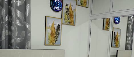 A hotel room with a bed, a clock, and artwork on the walls.