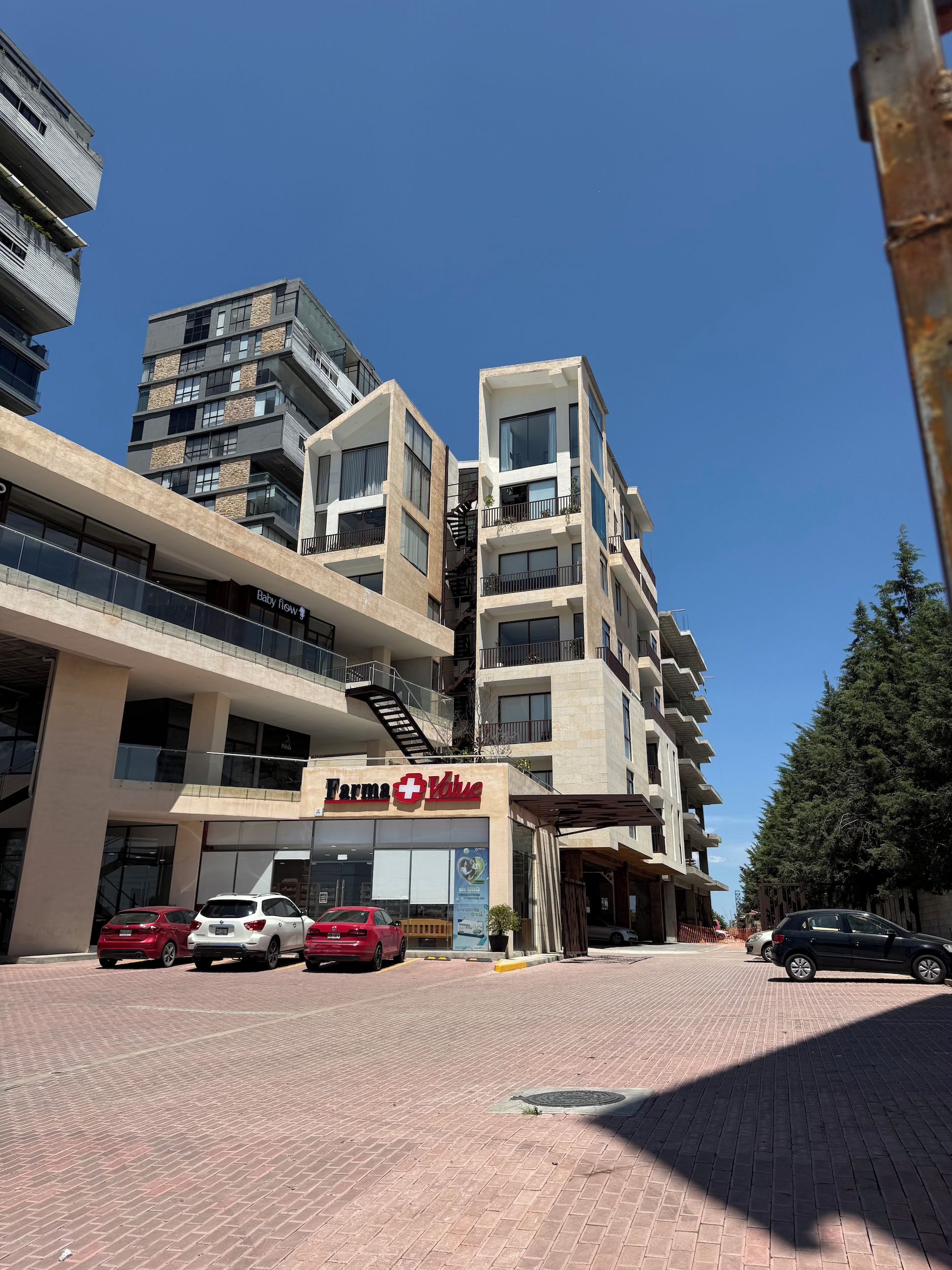Un edificio de varios pisos con un local comercial en la planta baja, una escalera visible y un estacionamiento con varios automóviles.