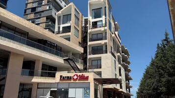 Un edificio de varios pisos con un local comercial en la planta baja, una escalera visible y un estacionamiento con varios automóviles.