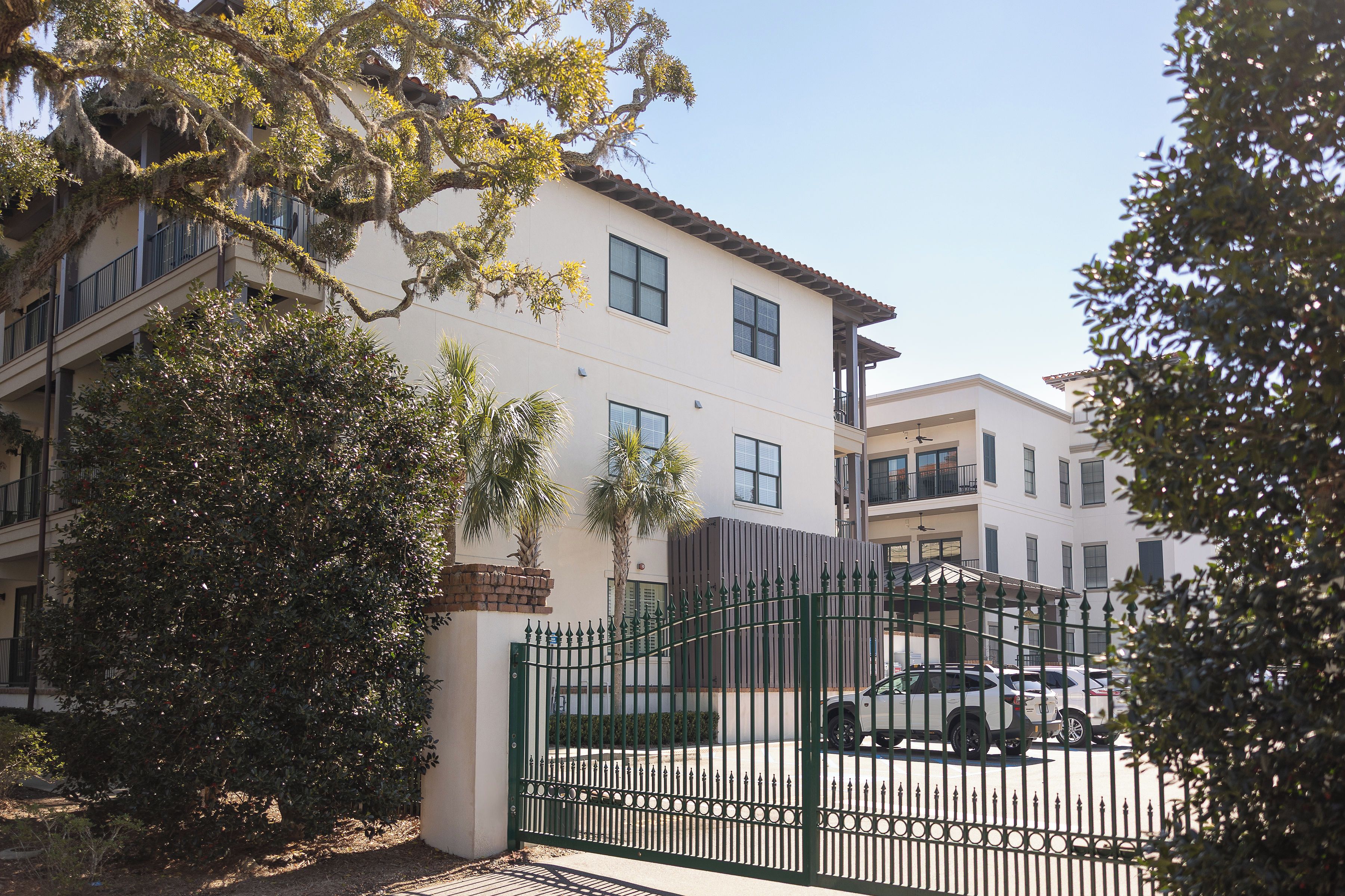 A multi-story residential building with a gated entrance, a balcony on the second floor, and a clear sky.
