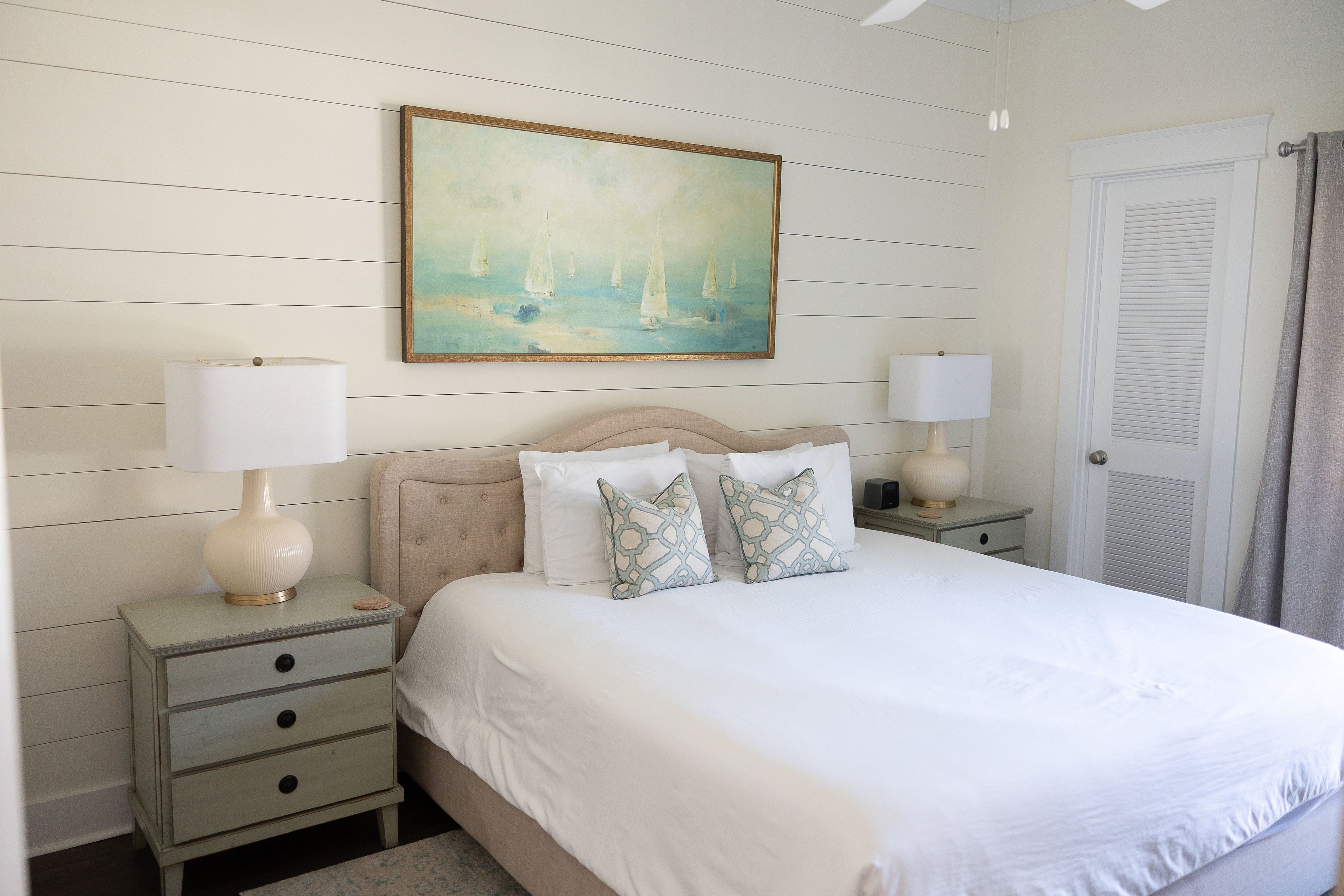 Une chambre à coucher avec un lit, deux tables de chevet, une commode, un tableau et une porte.