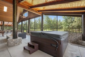 A covered outdoor area with a hot tub, stone seating, and a view of a wooded area.