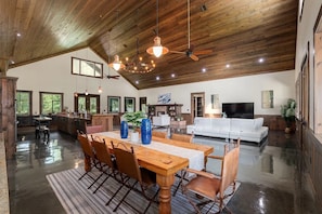 A spacious living area with a wooden ceiling, a dining table with chairs, a sofa, and a television. - Private 10-Acre Ranch Retreat — Sauna & Hot Tub (Morriston)