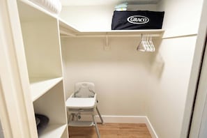 Habitació petita i estreta amb un canviador blanc per a nadons, una estant amb una bossa Graco i una prestatgeria penjant per a roba.