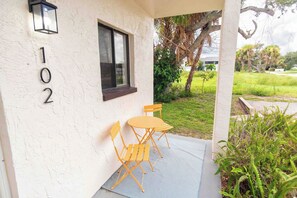A building with the number 102 on the wall, a window, and a patio area with a table and chairs. - Tropical Beach Oasis - Citrus (Cape Canaveral)