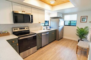 A modern kitchen with stainless steel appliances, a wooden ceiling, and a window providing natural light. - Tropical Beach Oasis - Citrus (Cape Canaveral)