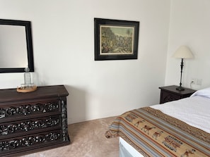 Een slaapkamer met een bed, een kaptafel, een lamp en een lijst met een foto aan de muur.