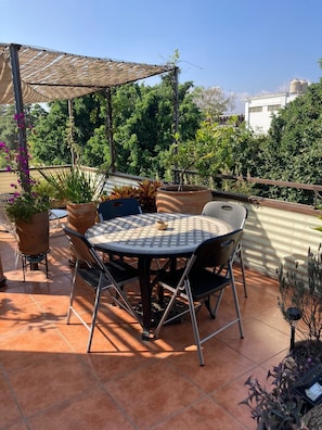 A patio with a round table and chairs, surrounded by potted plants and a pergola providing shade. - Fortaleza II Loft w AC Balcony Near Santo Domingo (Oaxaca)
