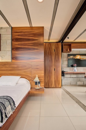A modern bedroom with a large bed, a nightstand, a wall-mounted TV, and a fireplace. - Oasis Loft AC Ubicacion (Oaxaca)