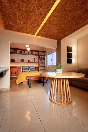 A modern living room with a wooden dining table, a sofa, and a built-in bookshelf. - La Fortaleza I Loft w AC Prime Historic Center Location (Oaxaca)