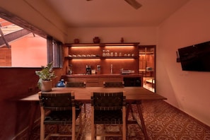 A dining area with a wooden table and chairs, a potted plant, and a kitchen area with shelves and appliances. - Rojo Stylish Apartment w AC and Premium Location in Historic Center (Oaxaca)