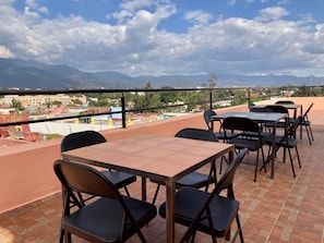 An outdoor terrace with tables and chairs, offering a view of a cityscape and mountains in the distance. - Rojo Stylish Apartment w AC and Premium Location in Historic Center (Oaxaca)