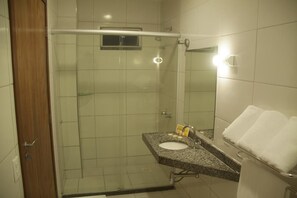 Un bany amb dutxa de vidre, un lavabo amb mirall i un suport per a tovallons.