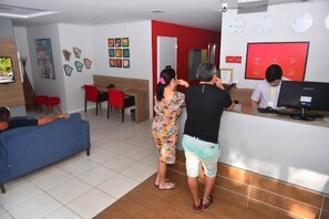 Un vestíbul d'hotel amb taulell de recepció, un sofà blau, zona de dinar i obres d'art a les parets.