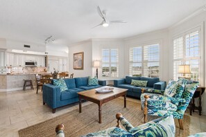 Ein geräumiges Wohnzimmer mit einer großen Sofagarnitur, einem Couchtisch und einem Essbereich, im Hintergrund eine Küche.