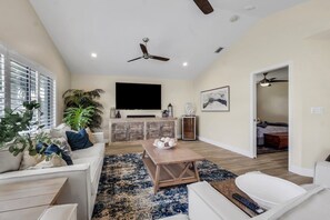 A spacious living room with a flat-screen TV, ceiling fan, and a large plant. - The Capes Cozy Corner 1016 SW Cape Pool Home, Gulf Access (Cape Coral)