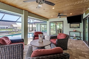 A covered patio area with wicker furniture, a round table, ceiling fans, and a view of a swimming pool. - The Capes Cozy Corner 1016 SW Cape Pool Home, Gulf Access (Cape Coral)