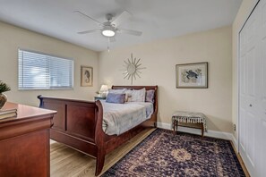 A bedroom with a wooden bed, a ceiling fan, a window with blinds, a wall-mounted mirror, and a small bench. - The Capes Cozy Corner 1016 SW Cape Pool Home, Gulf Access (Cape Coral)