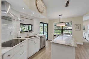 A modern kitchen with a central island, stainless steel appliances, and a large window providing a view of the outdoors. - The Capes Cozy Corner 1016 SW Cape Pool Home, Gulf Access (Cape Coral)