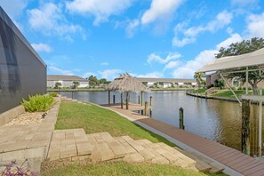 A waterfront property with a dock, a thatched-roof structure, and a modern building. - The Capes Cozy Corner 1016 SW Cape Pool Home, Gulf Access (Cape Coral)
