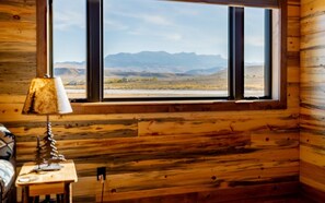 A room with wooden walls, a window with a view of mountains, a lamp, and a small table. - The Walkin Wyla- newly built barndominum (Cody)