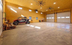 A spacious garage with a red ATV, wooden planks, and two large garage doors. - The Walkin Wyla- newly built barndominum (Cody)