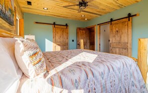 Ein Schlafzimmer mit einem Bett, Holztüren, einem Deckenventilator und einem Gemälde an der Wand.