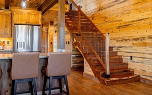 Ein Holzinnenraum mit Küchenzeile, zwei Barhocker und einer Holztreppe.