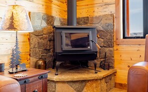 A wood-burning stove in a stone-walled room with a wooden ceiling and a window. - The Walkin Wyla- newly built barndominum (Cody)