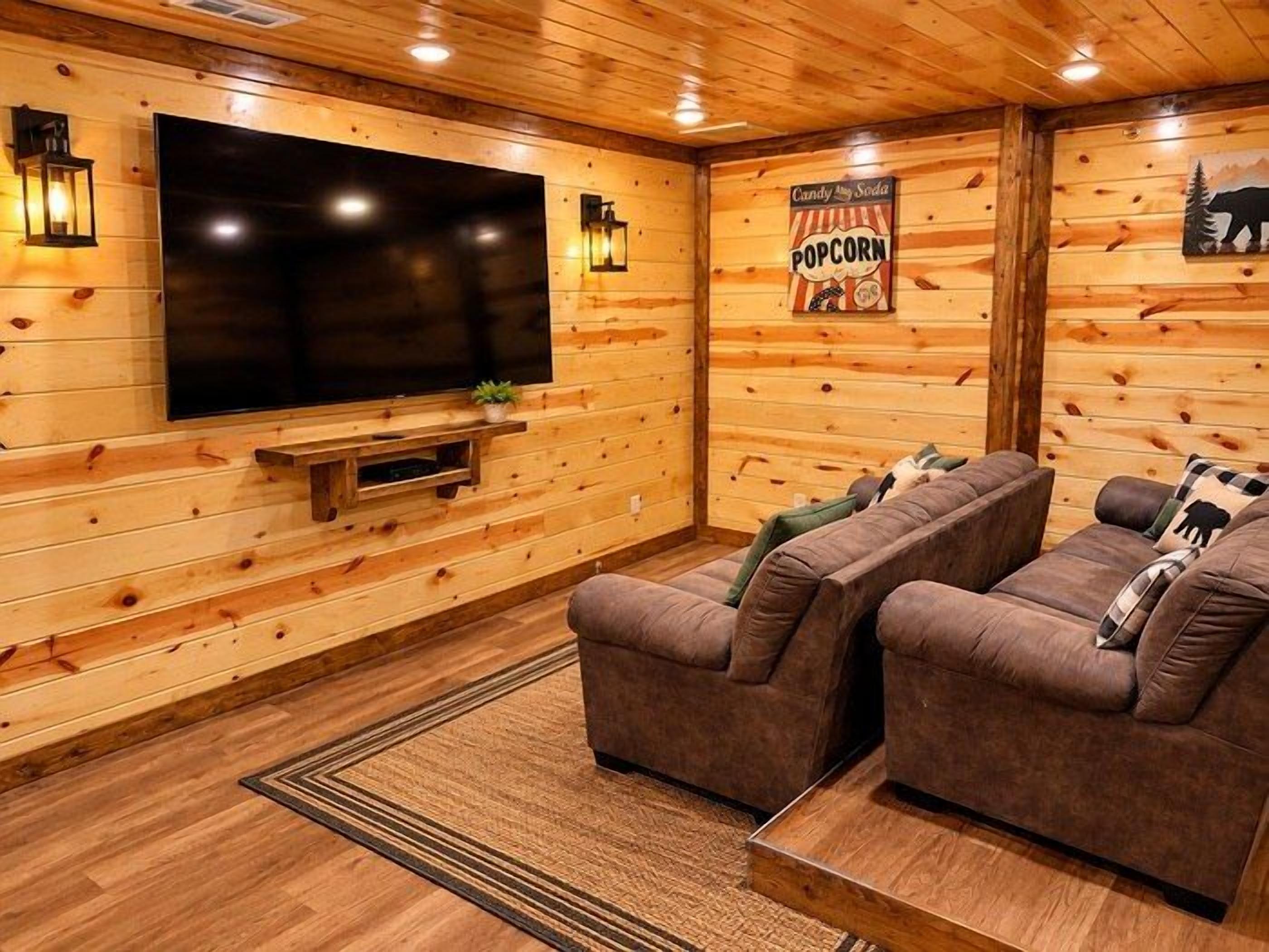 A cozy room with a large flat-screen TV, two sofas, a popcorn sign, and wooden walls.