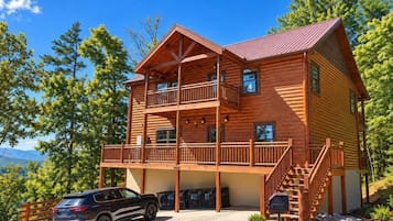 A two-story log cabin with a balcony, a staircase, and a car parked in front.