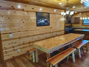A wooden interior with a long dining table and benches, a kitchen area, and a framed picture on the wall. - Private Pool, Hot Tub, Fire Pit, Game Room, Theater Room + Free Tix (Sevierville)