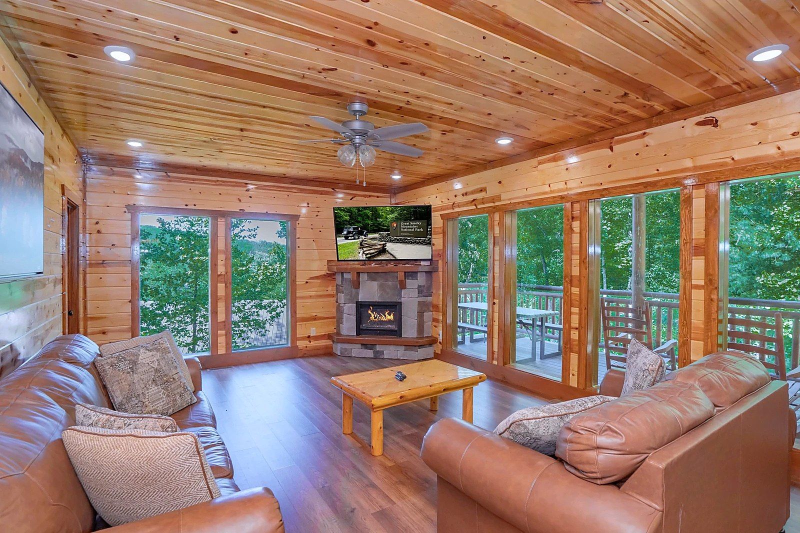 A cozy cabin interior with a fireplace, leather sofa, wooden flooring, and large windows.