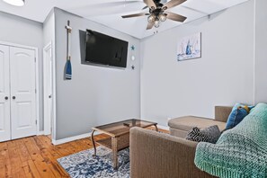 A modern living room with a ceiling fan, a flat-screen TV, a wicker sofa, and a patterned rug. - The Salt Flat — Waterfront Escape on Salt Lake with Private Pier (Rockport)