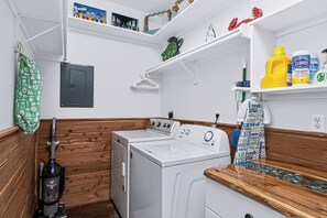 Un área de lavandería con lavadora, aspiradora y estante con productos de limpieza.