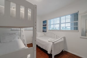 A room with bunk beds, a single bed, a window with blinds, and artwork on the wall. - Evie Mar | Keys Waterfront Escape + Pool & Dock & Kayak & Paddle board & Fishing (Marathon)