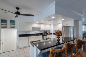 Una cocina moderna con armarios blancos, una isla central y un ventilador de techo.