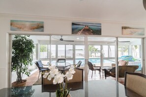 Una habitación con una mesa de vidrio, sillas, una planta en maceta y vistas a una piscina y una playa.