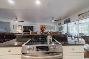 A kitchen with a central island, overhead ceiling fans, and a large window. - Evie Mar | Keys Waterfront Escape + Pool & Dock & Kayak & Paddle board & Fishing (Marathon)