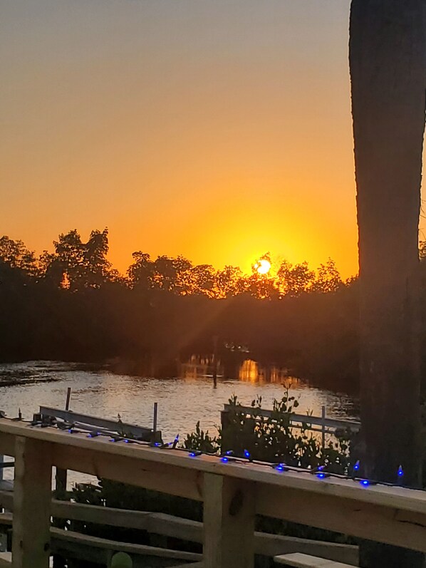A sunset over a body of water with a wooden railing and blue lights. - Cozy 2-bedroom waterfront manufactured home on Spring Creek with gulf access. (Bonita Springs)
