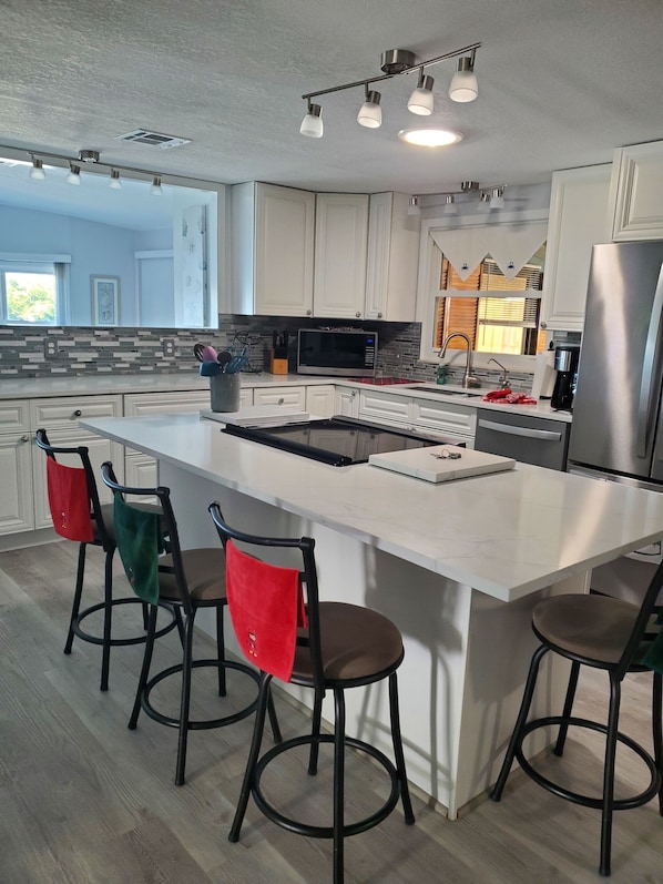 Cozinha moderna com ilha central, banquetas, geladeira de aço inoxidável e micro-ondas.