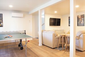 A room with a ping pong table, a sofa, a TV, and a poster on the wall. - WATERFRONT 4bd, 3.5ba Home w/ Private Dock, Hot Tub, Gas Fire Pit, 2 King Beds (Shelton)