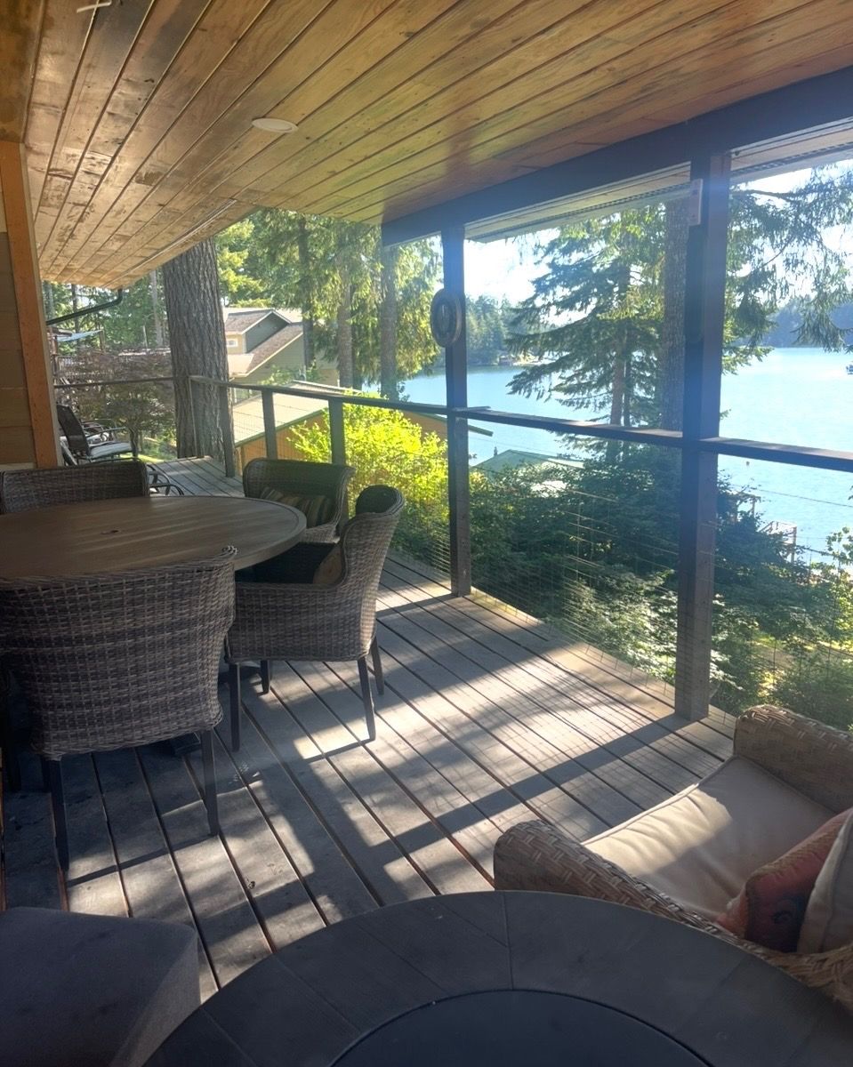 A covered outdoor deck with a table and chairs, overlooking a body of water and surrounded by trees.