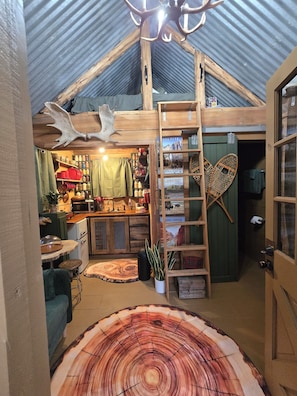 Un intérieur rustique avec un plafond en bois, une échelle et une grande table en bois dont le plateau présente un motif inspiré des cernes d’un arbre.