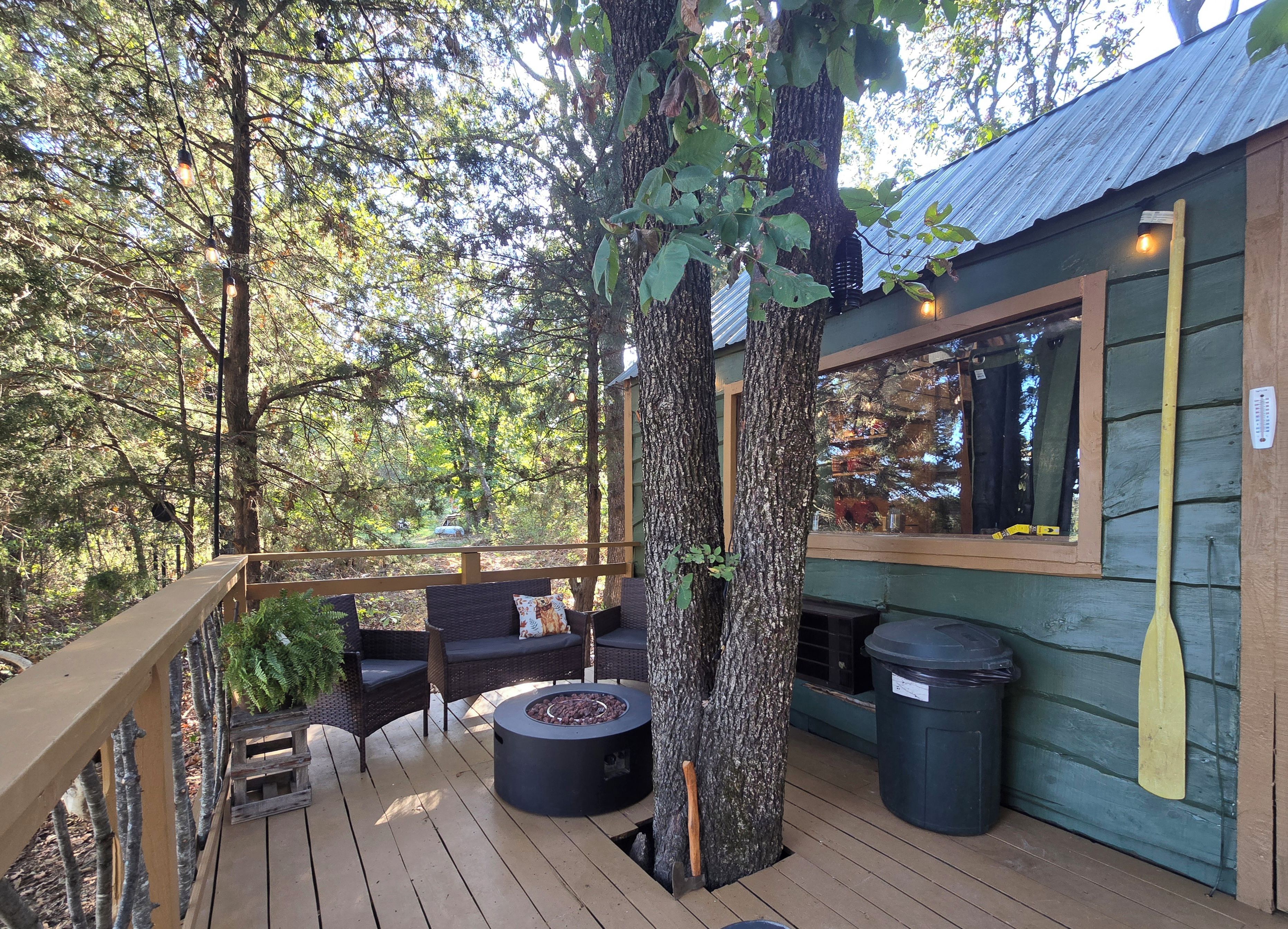 A wooden deck with outdoor seating, a fire pit, and a view of the surrounding forest.