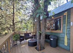 Une terrasse en bois avec des sièges d’extérieur, un foyer et une vue sur la forêt environnante.