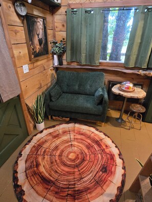 A cozy room with a wooden wall, a green sofa, a round wooden table, and a window with curtains.