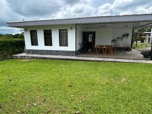 Um edifício térreo com varanda coberta, um pequeno gramado e céu claro.