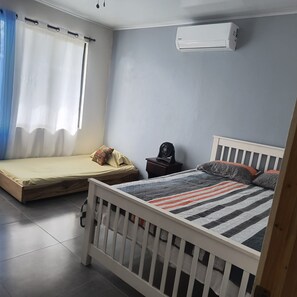 A bedroom with a single bed, a smaller bed, a bedside table, a fan, and an air conditioning unit. - New Listing (Provincia de Alajuela)